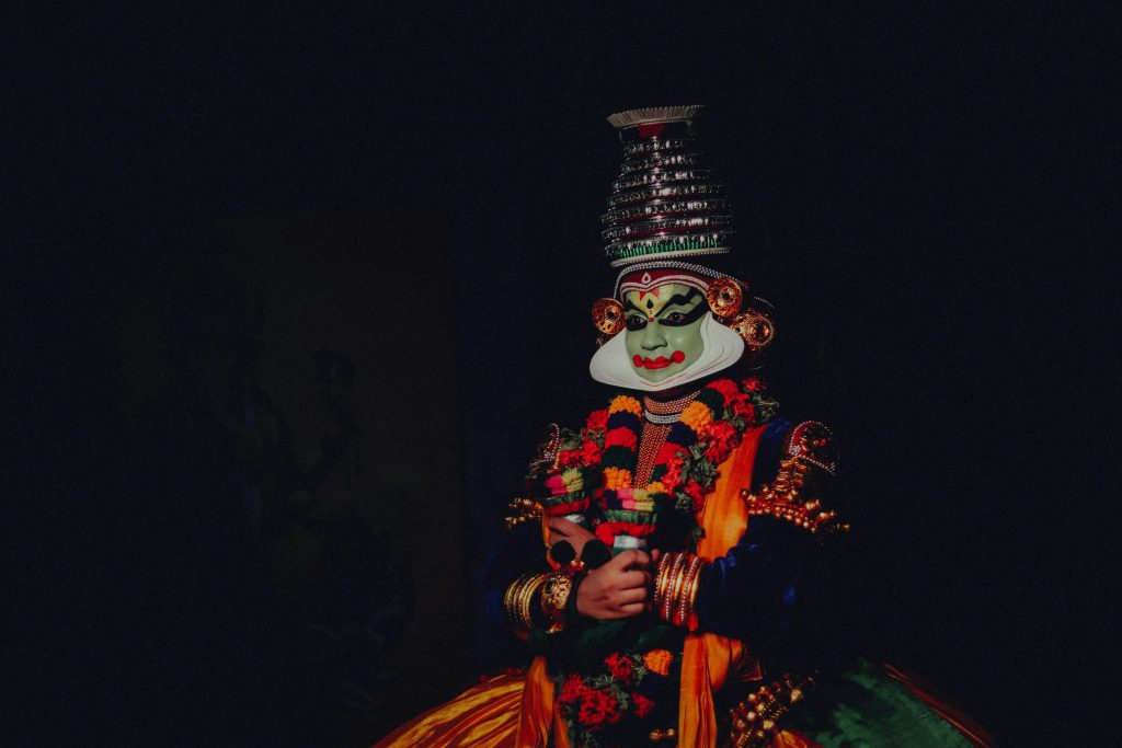 Colorful traditional Kathakali dancer with a distinctive mask on a black background.