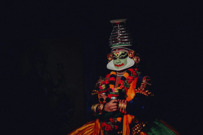Colorful traditional Kathakali dancer with a distinctive mask on a black background.
