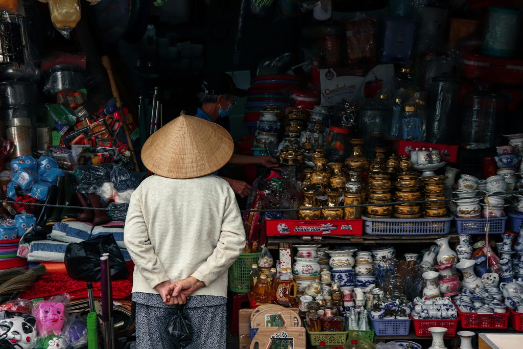 A person in traditional clothing stands at a vibrant market stall offering diverse crafts and goods.
